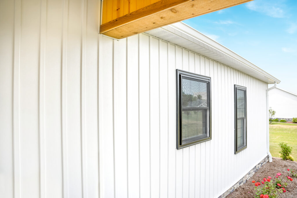Close-up of white board and batten vinyl siding with black-trimmed windows.