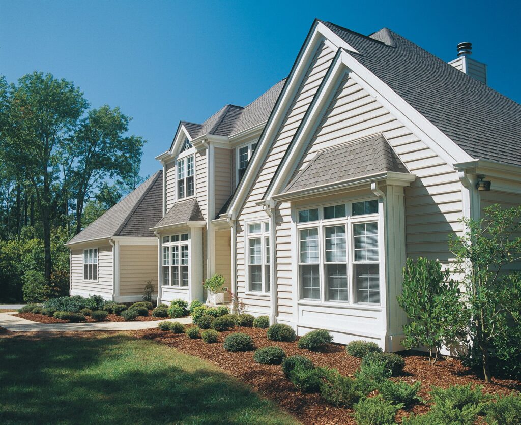 Cream vinyl lap siding on a large multi-gable home with white trim and landscaped entry.